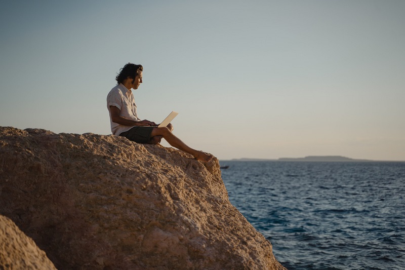A person working on their laptop in front of the sea