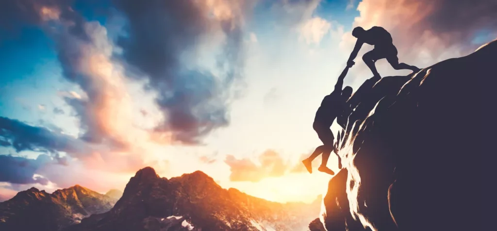 A man helping another climb the peak